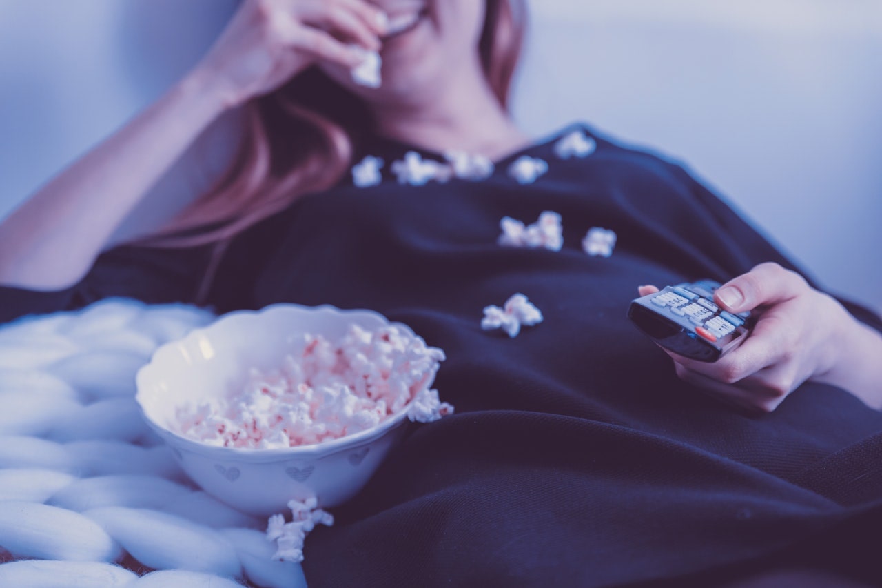 Woman holding remote control while eating popcorn
